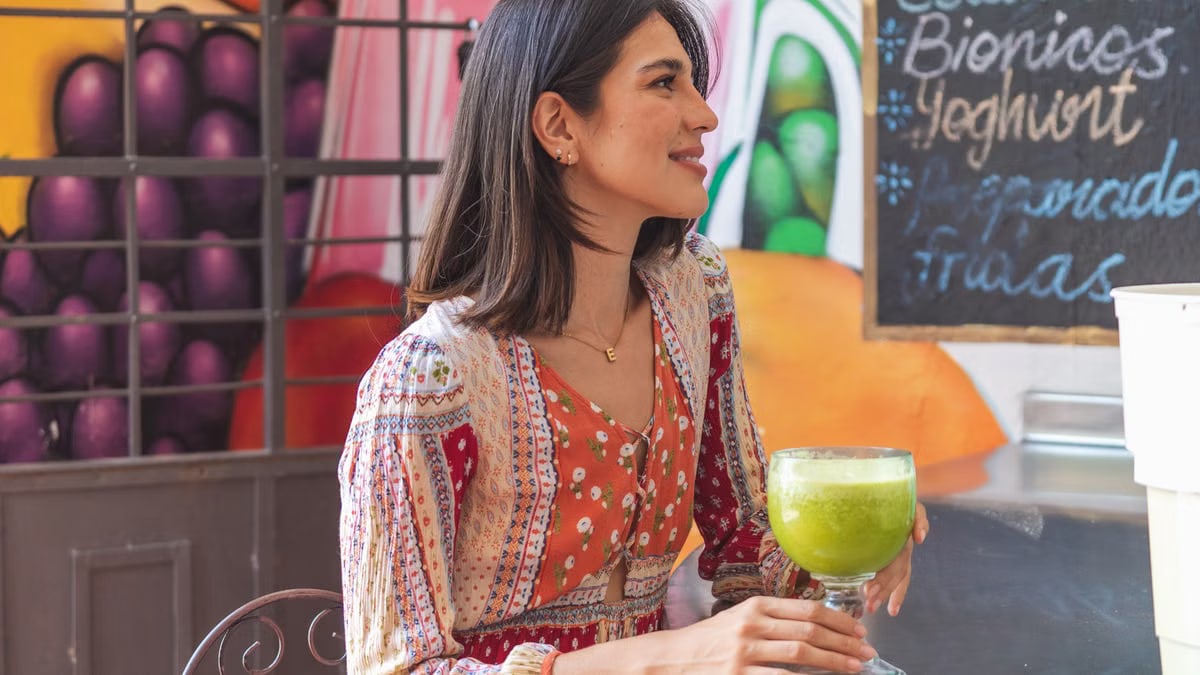 Woman holding a refreshing green juice in a lively café setting with colorful decor.