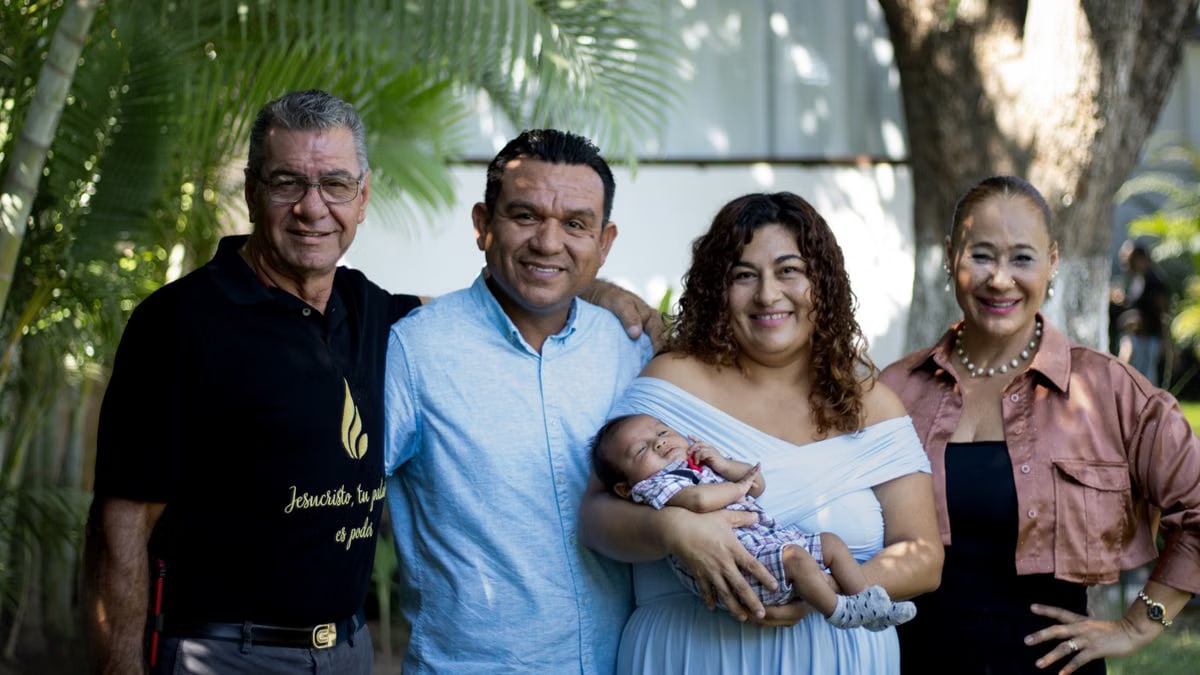 A happy family portrait featuring five adults and a baby outdoors.